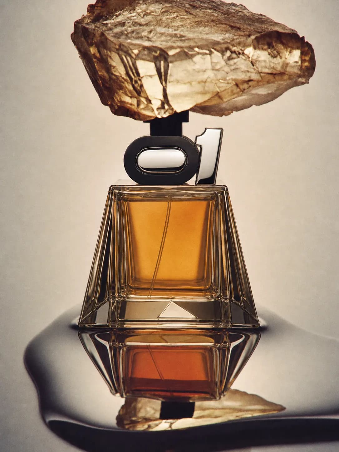 Golden flacon with a sculptural cap beneath a pale mineral surface.